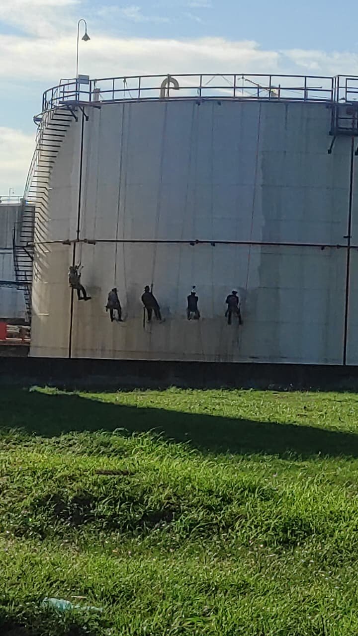 Cuadrilla en trabajo vertical preparando la pared de un tanque de almacenamiento